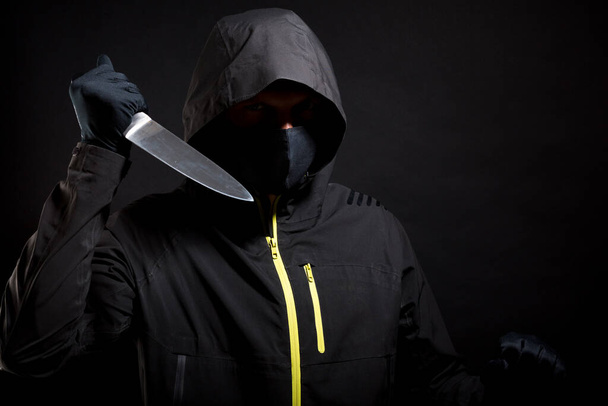 Unknown, indistinguishable bandit in black with knife attacks the victim with a knife. Concept: Crime because of crisis covid 19. Isolated on black background. Selective focus. - Photo, Image