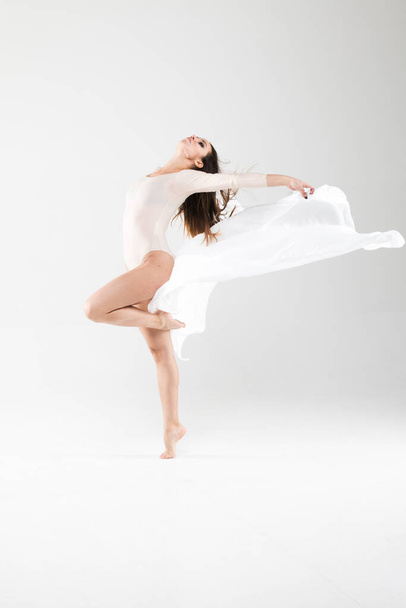 Beyaz arka planda kumaşla uçan bir dansçı kız. Fotoğraftaki duyguların ve duyguların ifadesi. Şefkat, dans, şehvet, bale, modern - Fotoğraf, Görsel