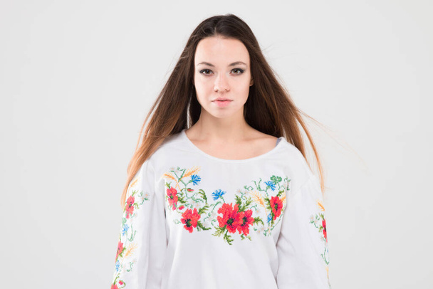 白い背景に民族ウクライナの刺繍シャツのブルネットの女の子。美しさ、故郷、感情、様式化された衣装、現代、シンボル、衣装、赤、伝統. - 写真・画像