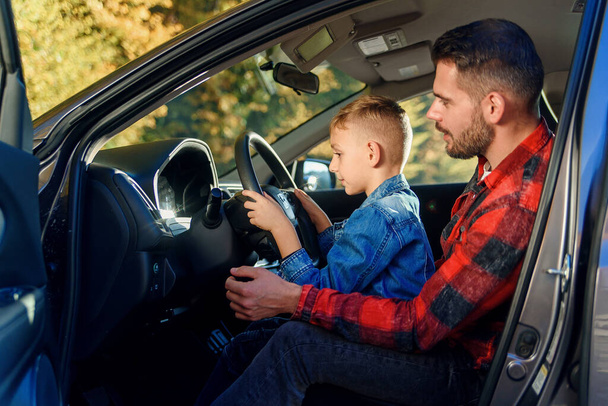 handsome father pointing on something while teaching teen son driving car - Photo, image