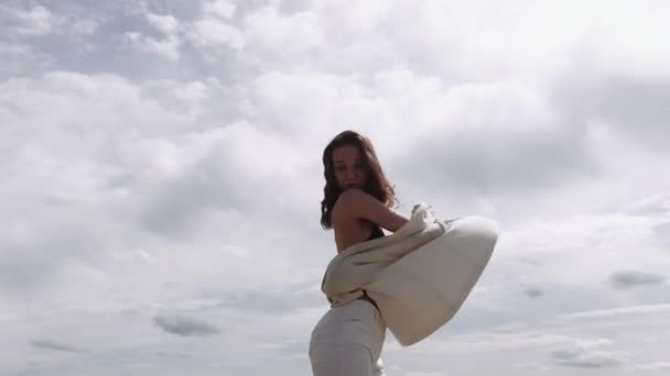 брюнетка дівчина чуттєво танцює на небі в білому костюмі і чорному баку зверху
 - Кадри, відео