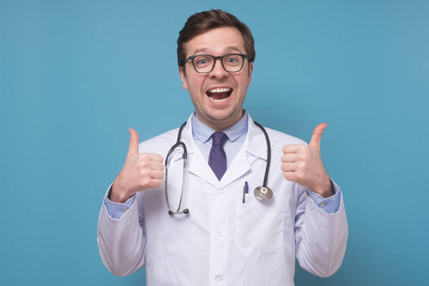 Vidám mosolygós orvos szemüvegben és orvosi köpenyben mutatja a hüvelykujját. - Fotó, kép