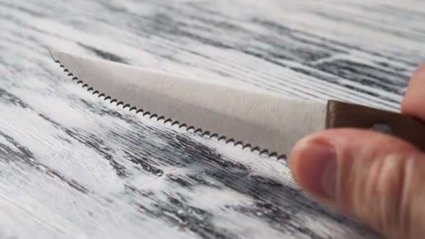 Zubatý nůž z nerezové oceli s dřevěnou rukojetí v ruce. Na krájení chleba. Na starém dřevěném povrchu. Hra světla - Záběry, video