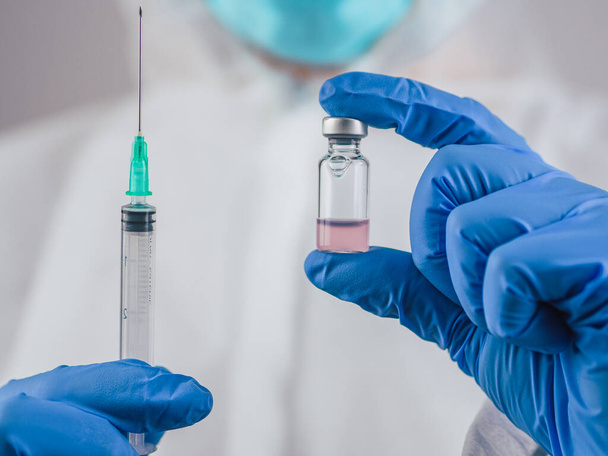 Um médico segura a vacina Covid-19 e uma injeção com luvas médicas azuis. Durante a crise do Coronavírus em quarentena. Conceito de cura para a saúde
. - Foto, Imagem