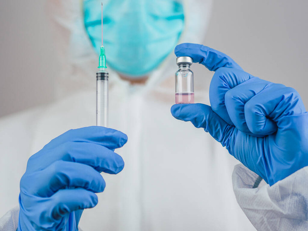 Egy orvos a Covid-19 vakcinát és egy kék orvosi kesztyűvel ellátott injekciót tart magánál. A karanténban a koronavírus krízis alatt. Az egészség gyógyításának koncepciója. - Fotó, kép