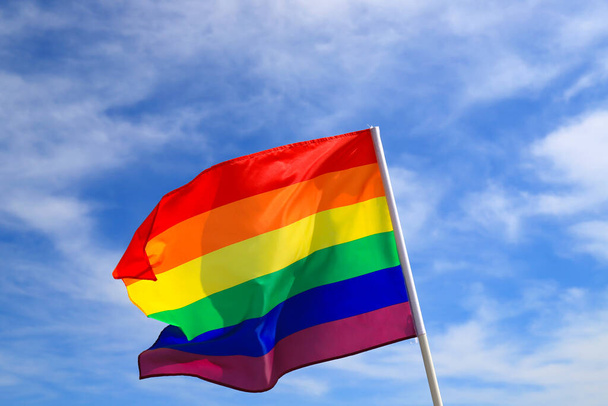 青い空に手を振っているLGBT組織の現実的な虹の旗。LGBTのプライドフラグには、レズビアン、ゲイ、バイセクシャル、トランスジェンダーの人々が含まれます。. - 写真・画像
