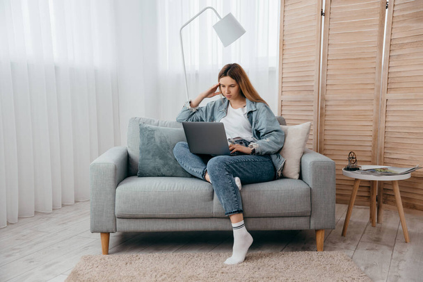 Μαθήτρια νεαρή κοπέλα ξαπλωμένη στον καναπέ στο σπίτι, κοιτάζει την οθόνη του φορητού υπολογιστή και να συμμετέχουν σε webinar να πάρει νέες γνώσεις ή την επικοινωνία με το φίλο μακρινή έννοια - Φωτογραφία, εικόνα