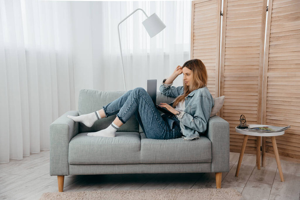 Студентська молода дівчина лежить на дивані вдома, дивиться на екран ноутбука і бере участь у вебінарі, отримуючи нові знання або спілкуючись з другом віддалено концепції
 - Фото, зображення