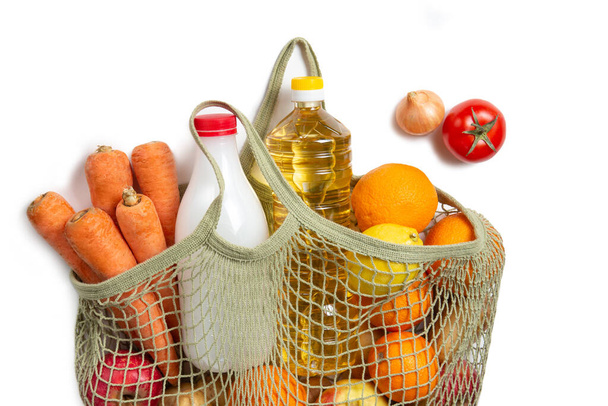 Vegetables, fruits, sunflower oil and milk in a string bag on a white isolated background. The concept of green shopping and proper nutrition. Environmental Protection. Delivery of products. Flat lay. - Foto, imagen