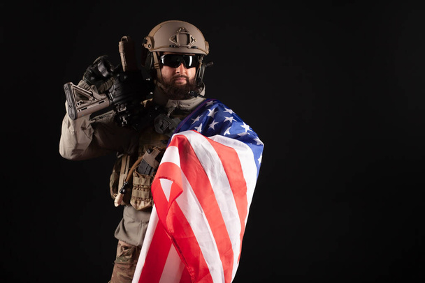 Американский современный спецназ на темном фоне, солдат в военной технике держит оружие и флаг Соединенных Штатов Америки, элитные войска
 - Фото, изображение