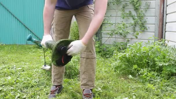 Egy férfi kertész megtisztít egy elektromos vágót, miközben az udvaron dolgozik, a nyers fűtől. Az önkormányzati szolgálatok és a magánalkalmazottak nyári munkája. - Felvétel, videó