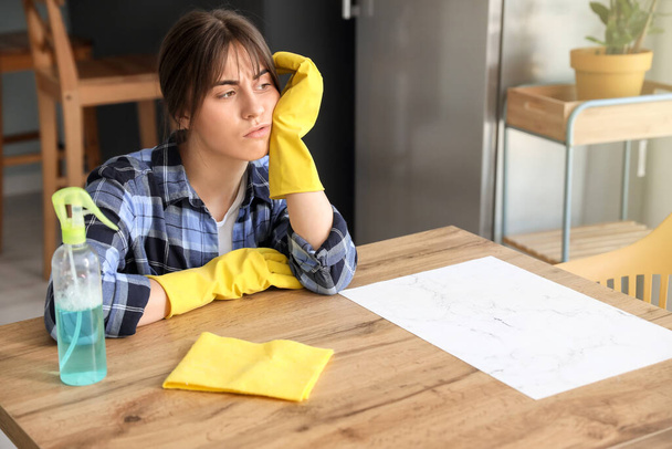 Mujer joven y cansada con artículos de limpieza en la cocina
 - Foto, imagen