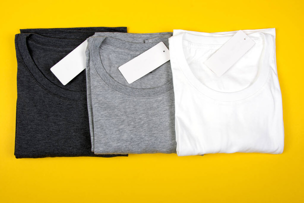Dunkelgraue, graue und weiße T-Shirts auf hellgelbem Hintergrund. - Foto, Bild