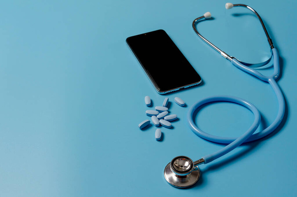 Телемедицина або телевізійна охорона здоров'я, концепція віддаленого відеочату лікаря зі смартфоном та стетоскопом на синьому фоні
. - Фото, зображення