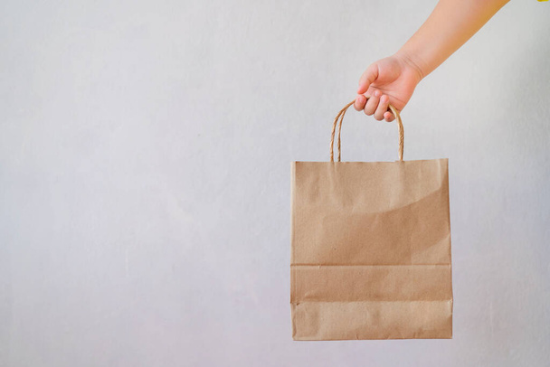 Asian girl is holding brown paper bag for mockup blank template. The background is a gray wall. - Foto, imagen
