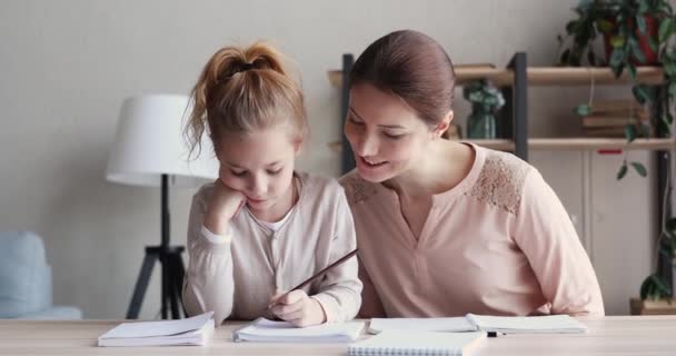 Smiling caring young mother helping little daughter doing school homework. - Séquence, vidéo