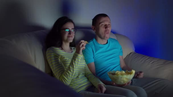 Facet z dziewczyną oglądającą zabawny film w telewizji, jedzącą chipsy i śmiejącą się - Materiał filmowy, wideo