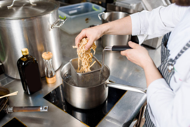 Nudle se dávají do pánve na kuchyni. Šéf vaří špagetové nudle na ramenovou polévku. Vaření ramenová polévka s masem, houbami, ředkvičkami, vejci. - Fotografie, Obrázek