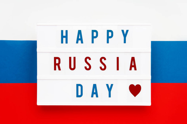 HAPPY RÚSSIA DIA escrito em lightbox no fundo bandeira russa. Data do dia da independência. Vista superior
. - Foto, Imagem