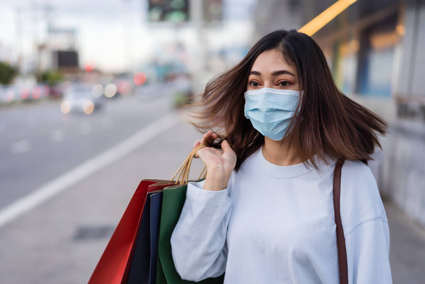 mladá žena držící nákupní tašku na ulici a nosící obličejovou masku na ochranu proti šíření pandemie koronaviru (covid-19), nový normální koncept - Fotografie, Obrázek