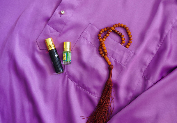 Imagen conceptual de la celebración eid adha. Cuentas de oración y perfume árabe en traje púrpura malayo con clavos en los ojales. Enfoque selectivo en cuentas de oración
. - Foto, imagen