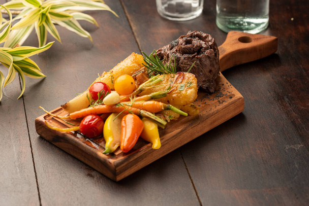 Tahtada sebzeli ve bulanık arka planlı düz demir etekli biftek. - Fotoğraf, Görsel