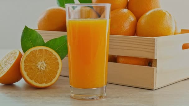 σωρός από φρέσκα πορτοκάλια σε ξύλινο κουτί και ένα ποτήρι χυμό - Πλάνα, βίντεο