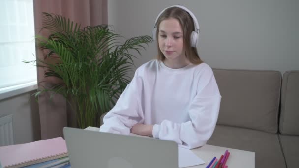 A beautiful girl is trained at home online with headphones on her head. - Filmagem, Vídeo