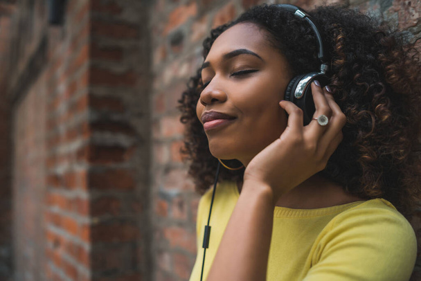 Portrait of young Afro american woman listening to music with headphones in the street. Outdoors. - Foto, Imagem