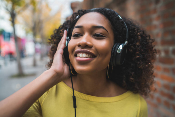 Portrait of Afro american woman smiling and listening to music with headphones in the street. Outdoors. - Zdjęcie, obraz
