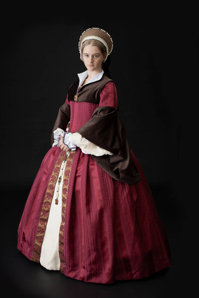Une femme Tudor en robe rouge et marron debout sur fond noir
 - Photo, image