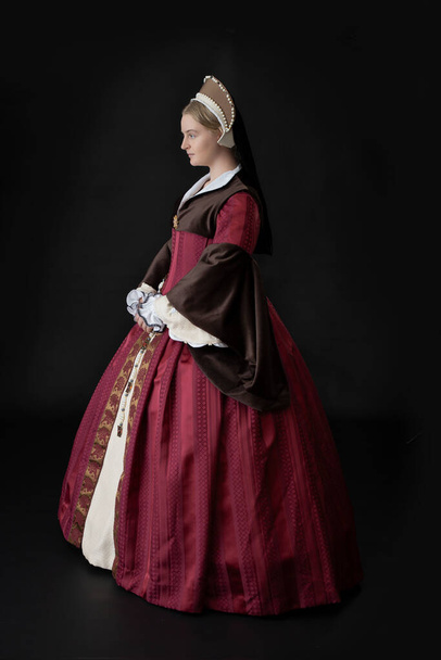 Μια γυναίκα Tudor σε ένα κόκκινο και καφέ φόρεμα στέκεται σε ένα μαύρο φόντο - Φωτογραφία, εικόνα