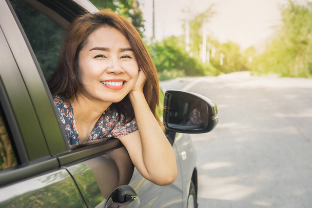 szczęśliwa Azjatka siedzi w samochodzie uśmiechnięta do aparatu fotograficznego, podróż samochodem podczas wakacji, wypożyczalnia samochodów koncepcja  - Zdjęcie, obraz