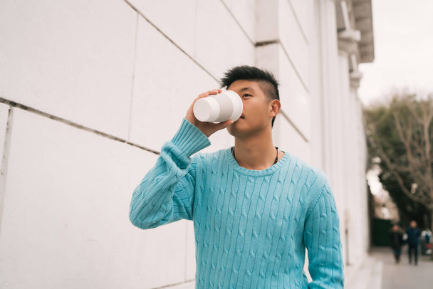 Portrait of young Asian man drinking a cup of coffee while walking outdoors in the street. Urban concept. - Φωτογραφία, εικόνα