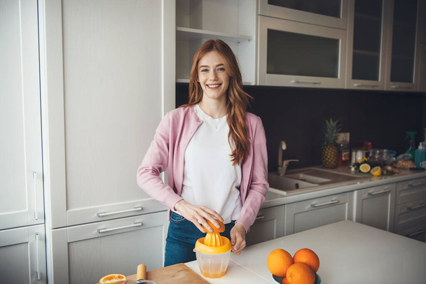 Ginger caucasian lady with freckles smiling at camera while squeezing fruits and making juice - Foto, immagini
