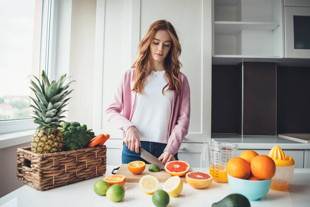 Ginger lady with freckles slicing fruits before squeezing the for juice - Photo, Image