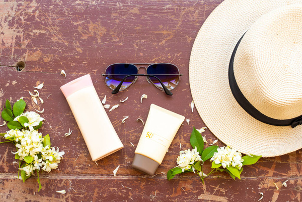 日焼け止めspf50,ボディローション化粧品スキンケアサングラス、帽子、白花のジャスミンのライフスタイル女性の夏の季節の配置でリラックスフラットレイスタイルを背景に木製  - 写真・画像