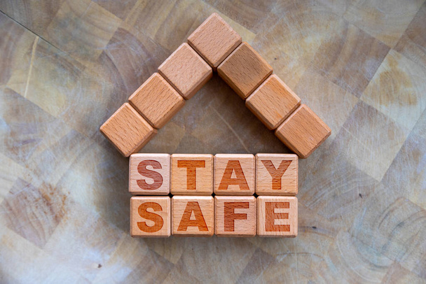 Stay home to stay safe due to Covid-19 coronavirus outbreak pandemic. Concept of self isolation or quarantine message engraved on wooden blocks on wood background with copy space. - Photo, Image