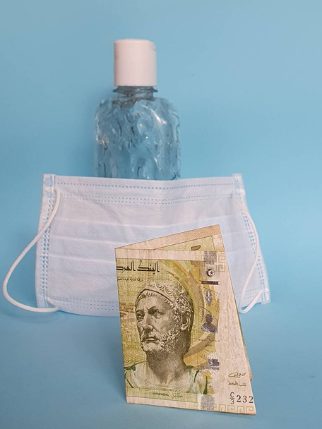 tunisian banknote of five dinars, face mask, bottle with gel alcohol and blue background - Фото, изображение
