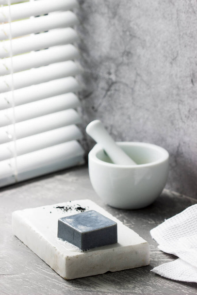 Ručně vyráběné mýdlo s aktivním uhlím na mramoru, uhlíkovým práškem a bavlněným ručníkem na šedém pozadí. - Fotografie, Obrázek
