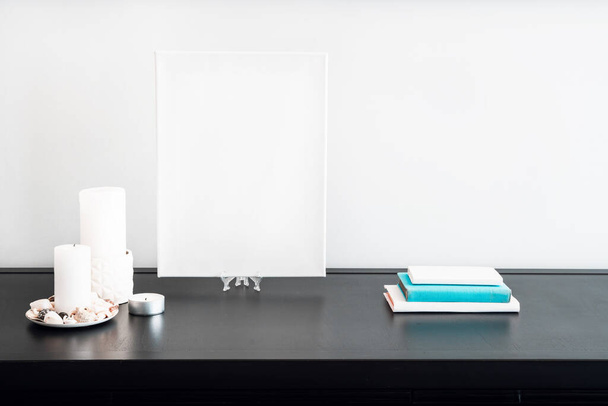 Blank white canvas for artist's mock-up, candles, white and blue books on black table and white wall. Minimalism style. - Fotografie, Obrázek