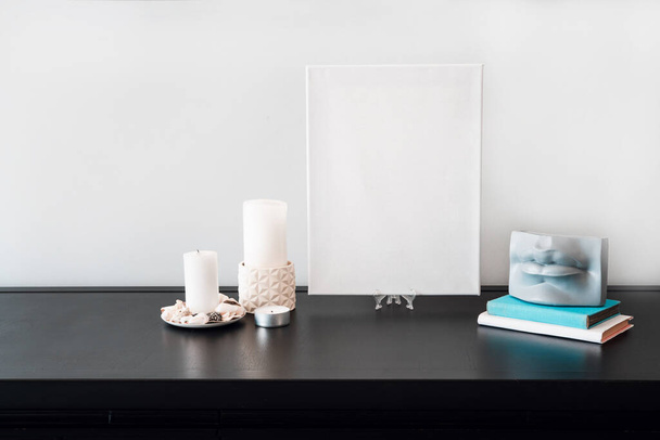 Interior design of room, blank white canvas for artist's mock-up, lips shaped vase with dry flowers bouquet, candles, white books on black table and white wall. Minimalism style. - Photo, Image