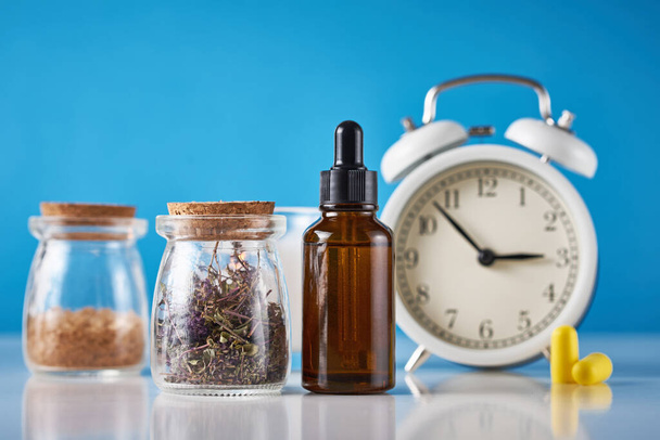 Herbal medicine for treat depression and insomnia concept. Alarm clock, medicine herbs and aromatherapy oil on blue background - Photo, Image