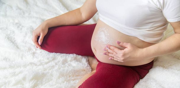 Беременная женщина мажет кремом от растяжек. Селективный фокус. люди
. - Фото, изображение