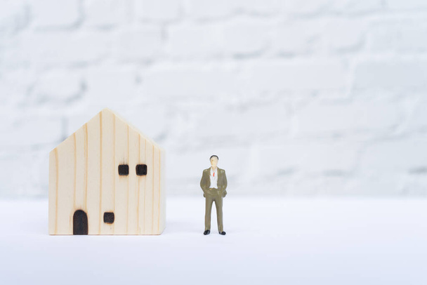 Wooden house and miniature businessman on white table. Financial concept - Photo, Image