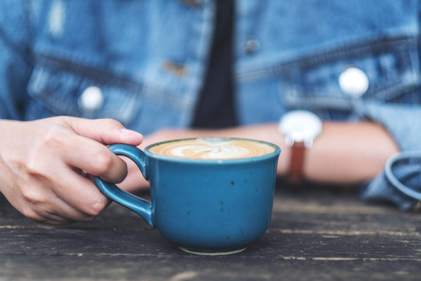 Closeup image of a woman holding a blue cup of hot coffee on wooden table - 写真・画像