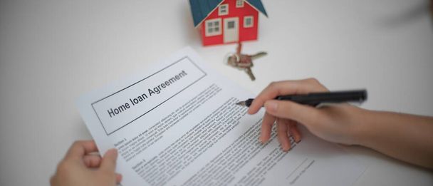 Közelkép egy nő olvas lakáshitel megállapodás, hogy fontolja meg, mielőtt aláírja a szerződést az asztalra a ház modell  - Fotó, kép