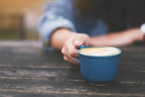 Nahaufnahme einer Frau mit einer blauen Tasse heißen Kaffees auf einem Holztisch - Foto, Bild