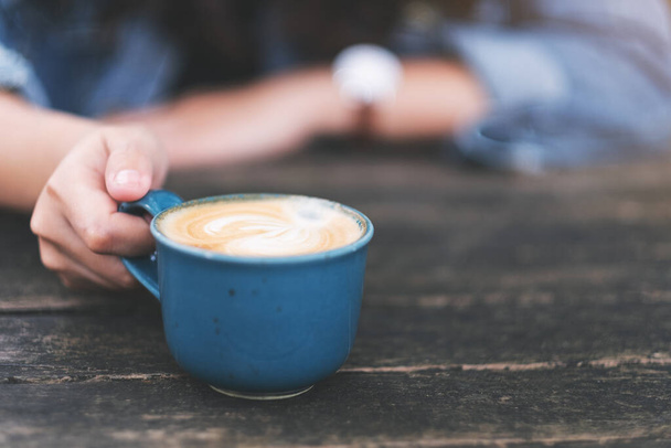 Közelkép egy nőről, aki egy kék csésze forró kávét tart a fa asztalon. - Fotó, kép
