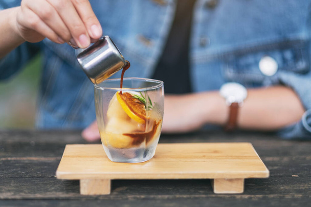 A woman pouring espresso shot into a glass of ice and lemon - Photo, Image